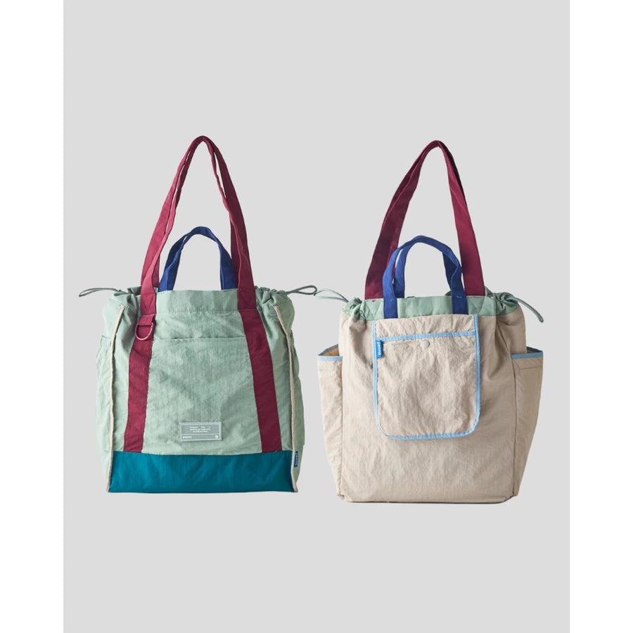 Reversible tote bag by Muhajir Project displayed in two sides, showing dual-color design with maroon and light green combination on one side and grey with light blue lining pocket on the other. This versatile women’s bag features long shoulder straps, side drawstring details, and a functional front pocket, highlighting its practical and stylish two-in-one design.