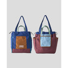 Reversible tote bag by Muhajir Project displayed in two sides, showing dual-color design with blue and brown combination on one side and maroon with light blue pocket on the other. This versatile women’s bag features long shoulder straps, side drawstring details, and a functional front pocket, highlighting its practical and stylish two-in-one design.