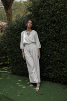 Woman in a white top and linen pants by Kasyalia standing in a garden setting