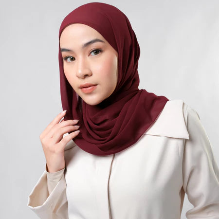 Woman wearing a maroon pashmina hijab by Tantri Namirah Official against a light gray background