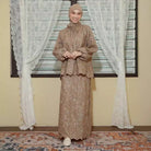 Woman in a beige traditional outfit by Lozy Hijab standing in front of a window with white curtains.