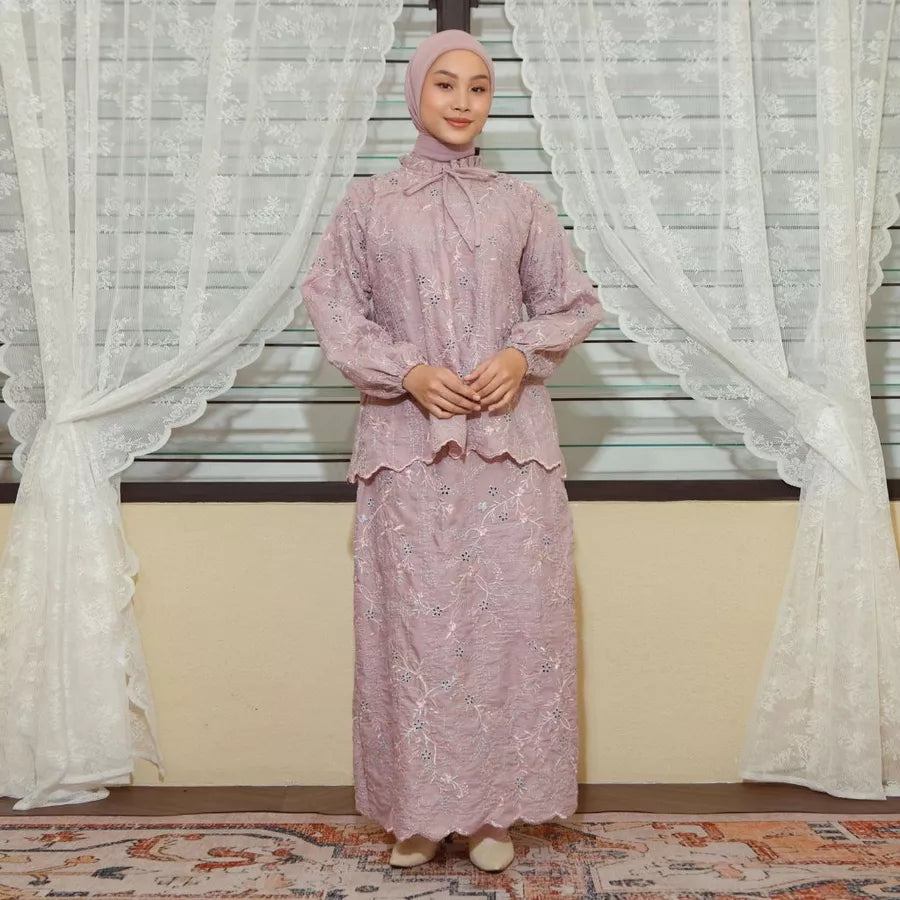 Woman in a pink traditional outfit by Lozy Hijab standing in front of white curtains.