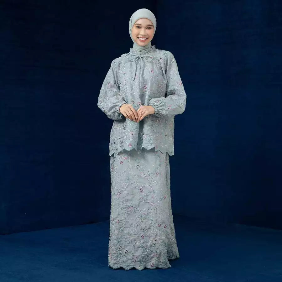 Woman wearing a light gray traditional outfit by Lozy Hijab with a matching headscarf against a dark blue background