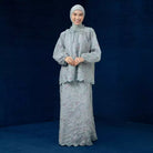 Woman wearing a light gray traditional outfit by Lozy Hijab with a matching headscarf against a dark blue background