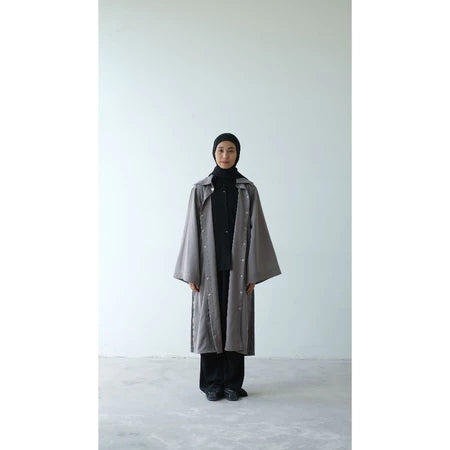 Person wearing a long gray coat from Rashawl and black hijab on a white background