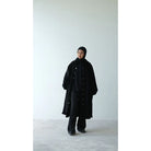 Person wearing a long black coat by Rashawl and black pants on a white background