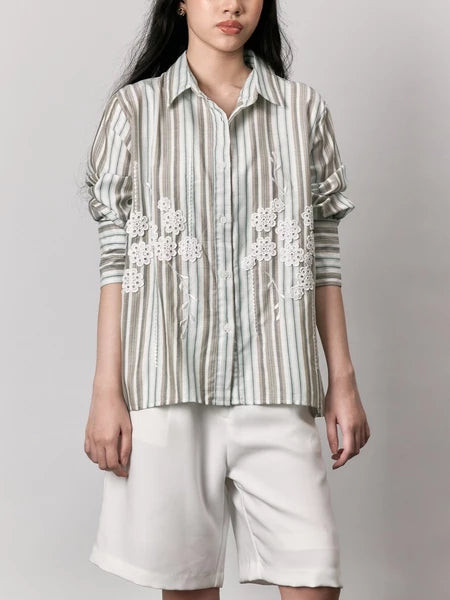 Woman wearing a striped shirt with floral embroidery and white shorts by Studio Tui on a plain background