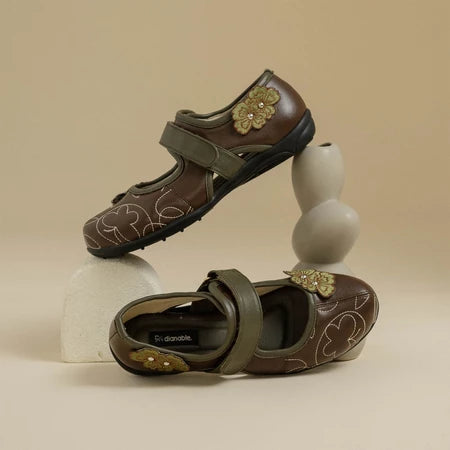 Pair of dark brown flat shoes with floral designs by Dianable on a beige background