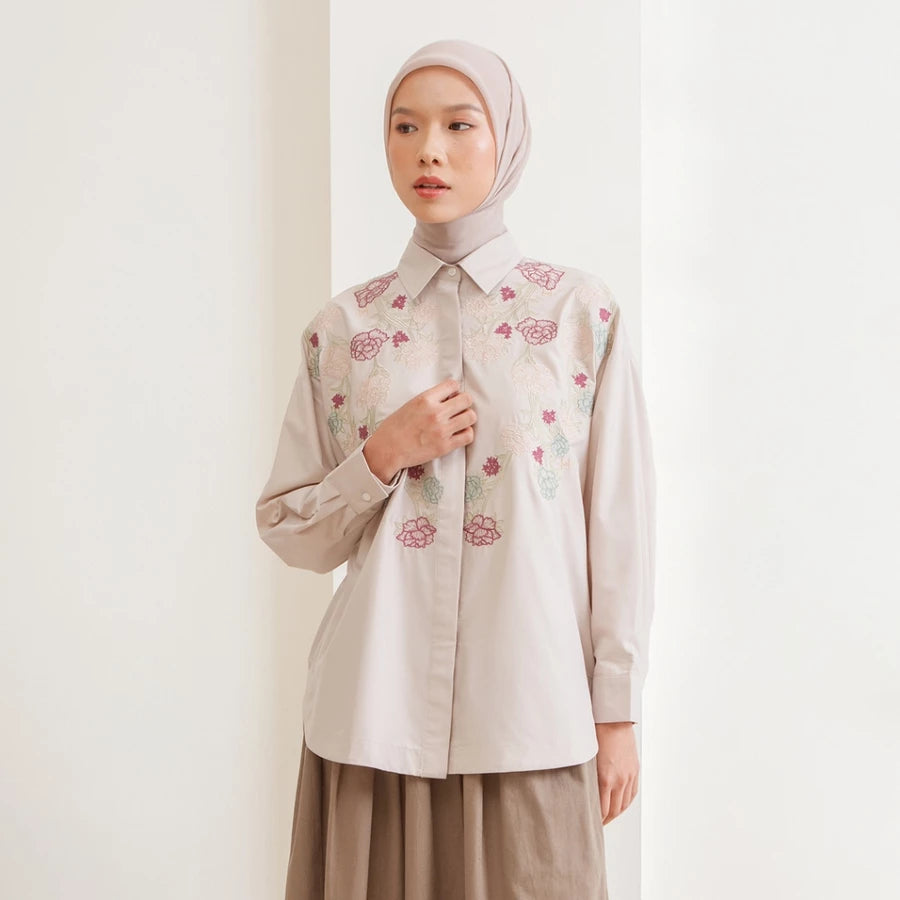 Woman wearing a beige shirt with floral embroidery by Hijabchic against a white background