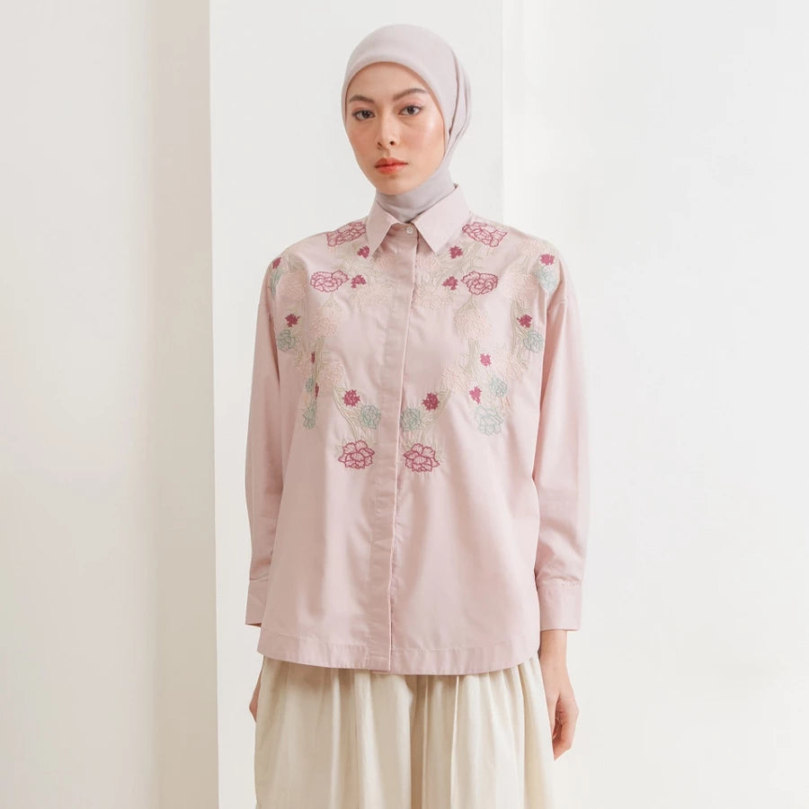 Woman wearing a light pink shirt with floral embroidery by Hijabchic on a plain background