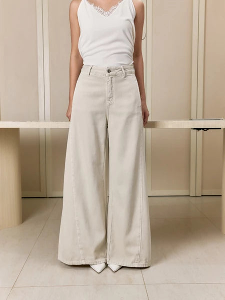 Person wearing a white sleeveless top and white wide-leg jeans pants by Studio Tui in a minimalistic setting.