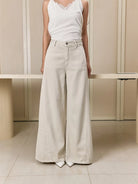 Person wearing a white sleeveless top and white wide-leg jeans pants by Studio Tui in a minimalistic setting.