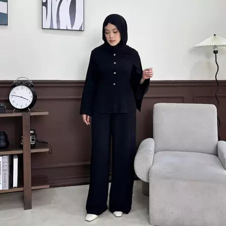Person wearing a black outfit by Renaette in a room with a clock and chair.