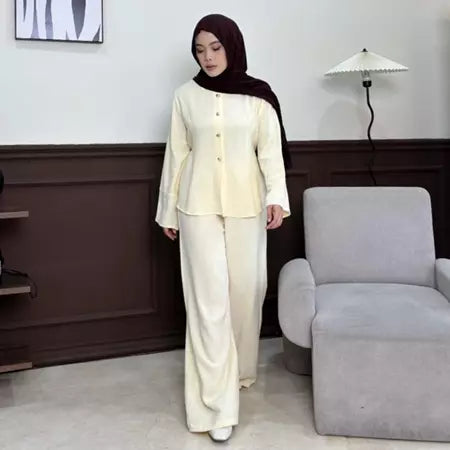 Woman in a cream outfit by Renaette standing in a room with a gray chair and white wall.