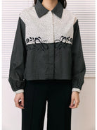 A woman wearing a long-sleeve shirt by Studio Tui with a color-blocked design: a cream and black micro-dot pattern on the upper chest and shoulders, solid black sleeves, and a black-and-white geometric pattern across the lower half. She is also wearing black pants.