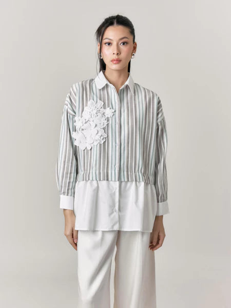 Woman wearing a striped shirt with floral details and white pants by Studio Tui on a plain background