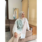 Person wearing a white shirt with green and beige accents by Abame and beige hijab indoors.