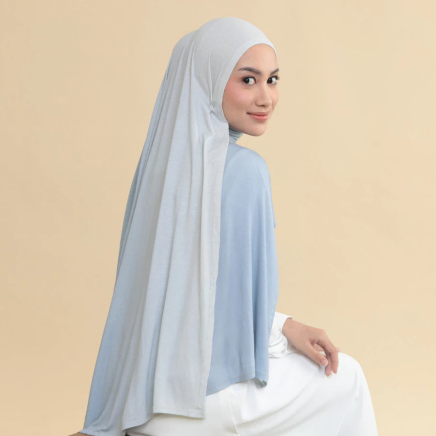 Woman wearing a light blue hijab shawl by Lozy Hijab and white outfit on a beige background