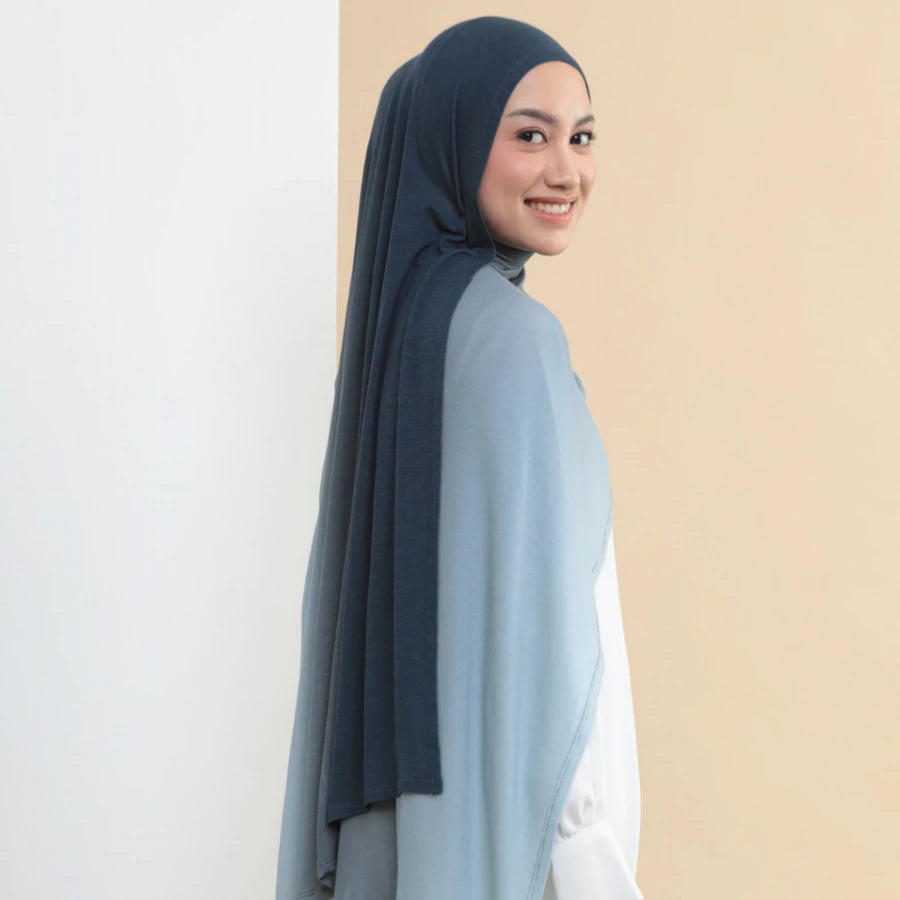 Woman wearing a dark blue hijab shawl by Lozy Hijab and light blue top on a beige background