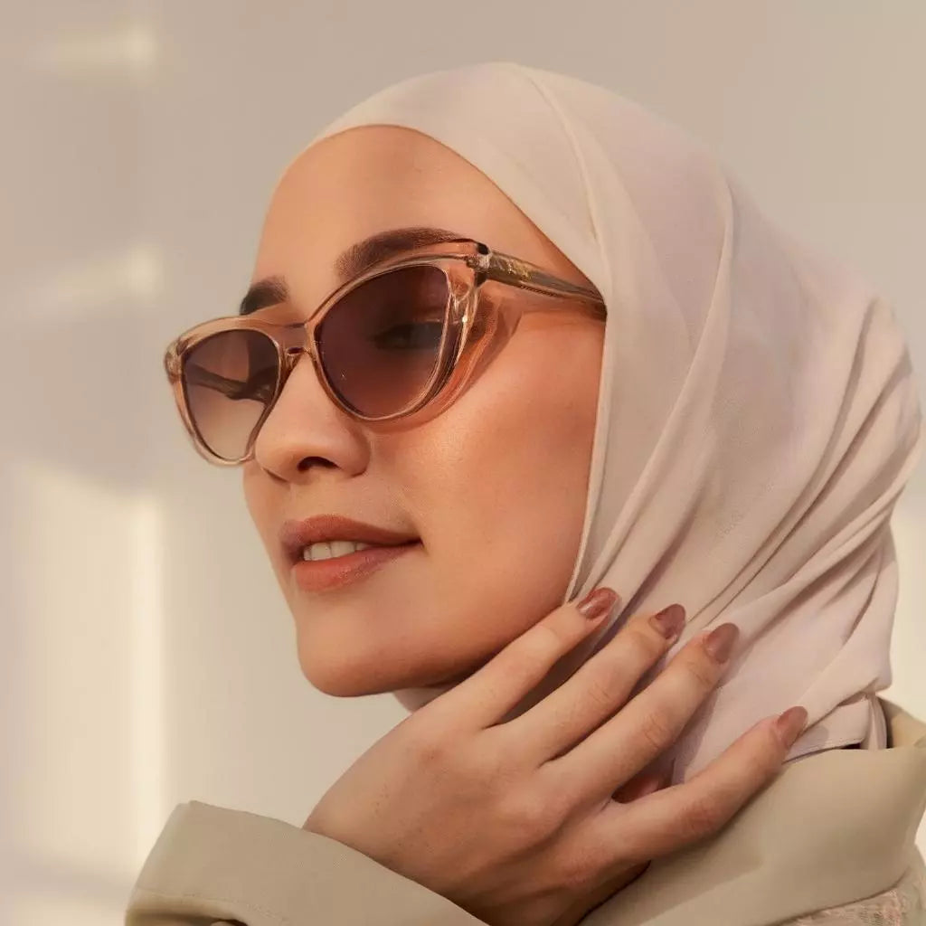 A woman wearing a beige headscarf and stylish sunglasses from HSF Eyewear with a cat-eye shape in a champagne gold color.