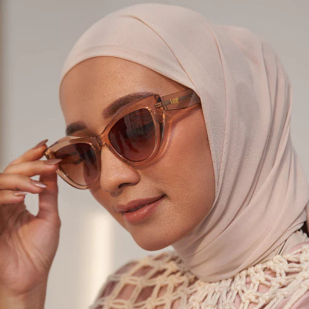 A woman wearing a beige headscarf and stylish sunglasses from HSF Eyewear with a cat-eye shape in a champagne color.