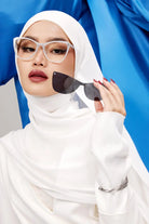 A woman wearing a white hijab and white outfit is showcasing a pair of acetate frame sunglasses with a cateye shape and clip-on polarized lenses from HSF Eyewear.