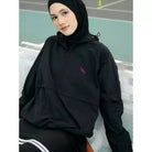 Person wearing a black windbreakers by Haidee Orlin with a logo on a sports court