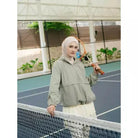Person wearing a sage green windbreakers by Haidee Orlin with a logo on a sports court