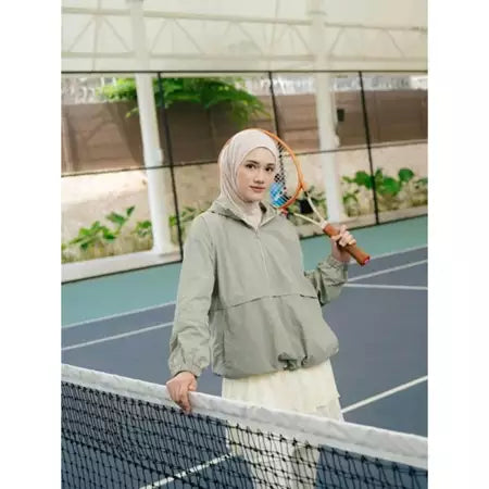 Person wearing a sage green windbreakers by Haidee Orlin with a logo on a sports court