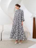 Woman wearing a long gray floral dress by Kasa Heritage with white floral pattern in a modern interior setting.