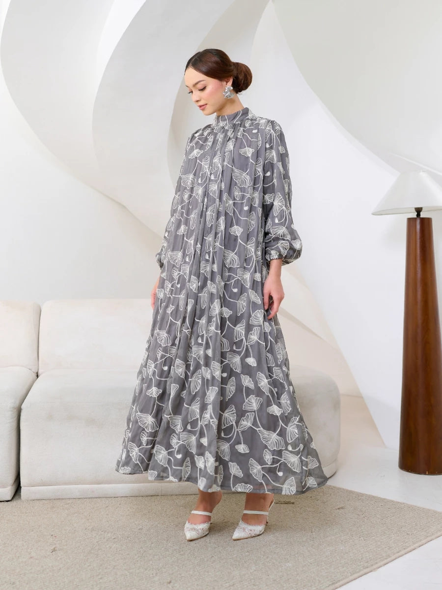 Woman wearing a long gray floral dress by Kasa Heritage with white floral pattern in a modern interior setting.
