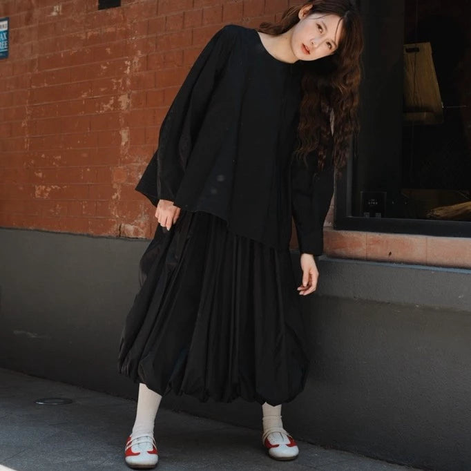 Person wearing a black blouse by Yestoday with white shoes against a brick wall.