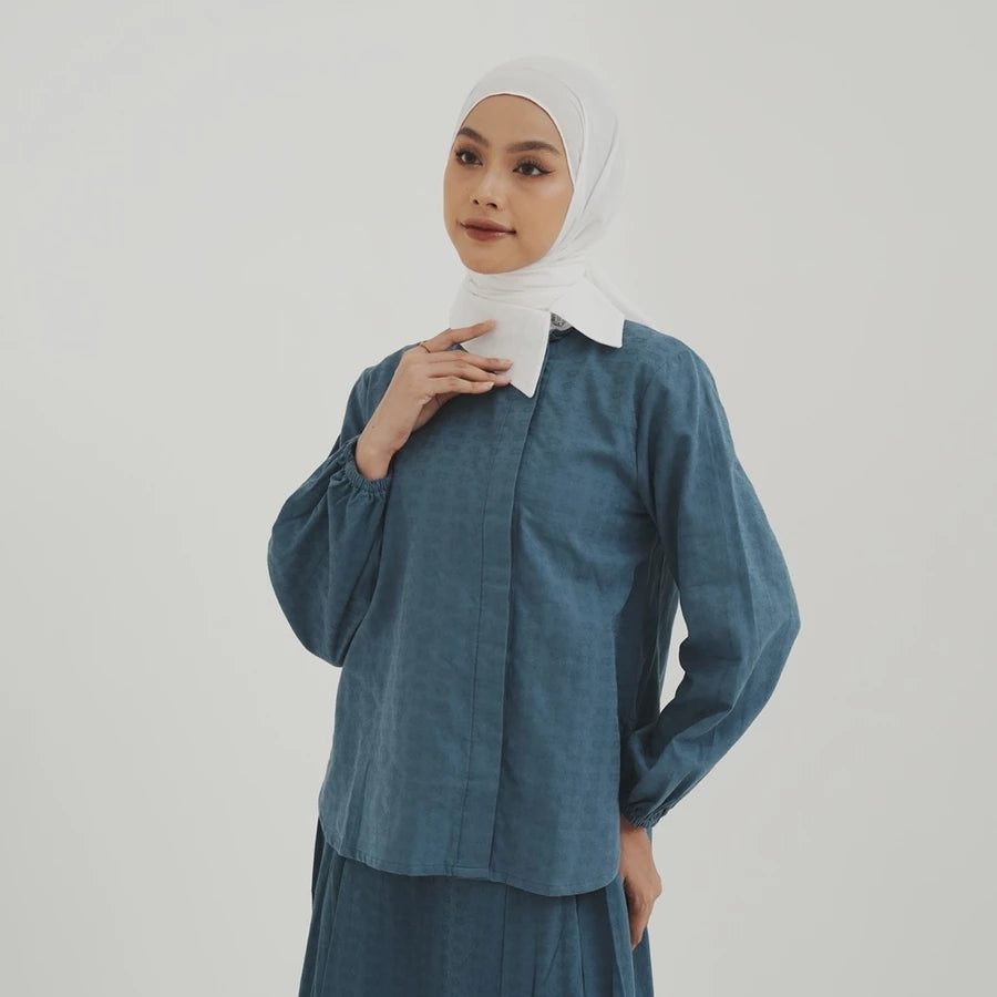 Woman wearing a blue denim shirt by Tunique with a white hijab on a plain background