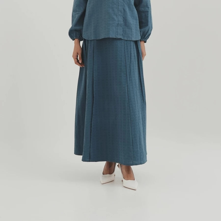 Person wearing a teal outfit with a long denim skirt by Tunique on a light gray background