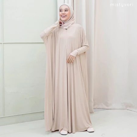 Woman wearing a beige hijab and dress by Mistyvori standing against a white curtain.