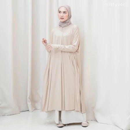 Woman wearing a beige long-sleeve tunic by Mistyvori and hijab against a white curtain background