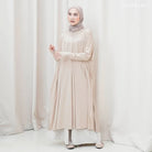 Woman wearing a beige long-sleeve tunic by Mistyvori and hijab against a white curtain background