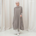 Woman wearing a long, light gray tunic by Mistyvori with a matching hijab against a white curtain background.