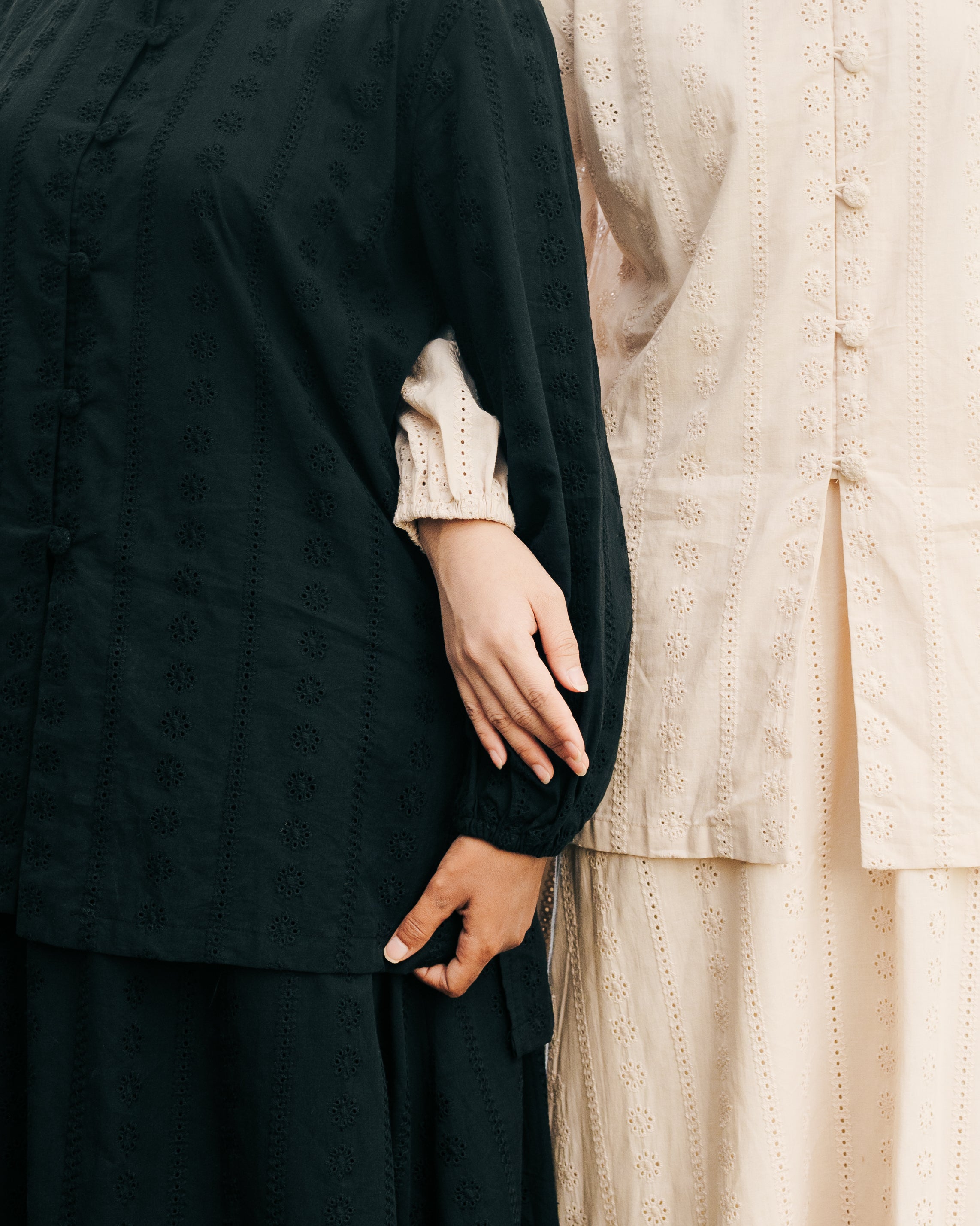 Two people wearing black and light brown long-sleeve tunic with a close-up of their hands.