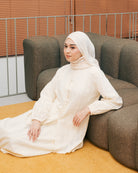 Woman in a broken white tunic from Atala Scarves sitting on a brown couch with a neutral background