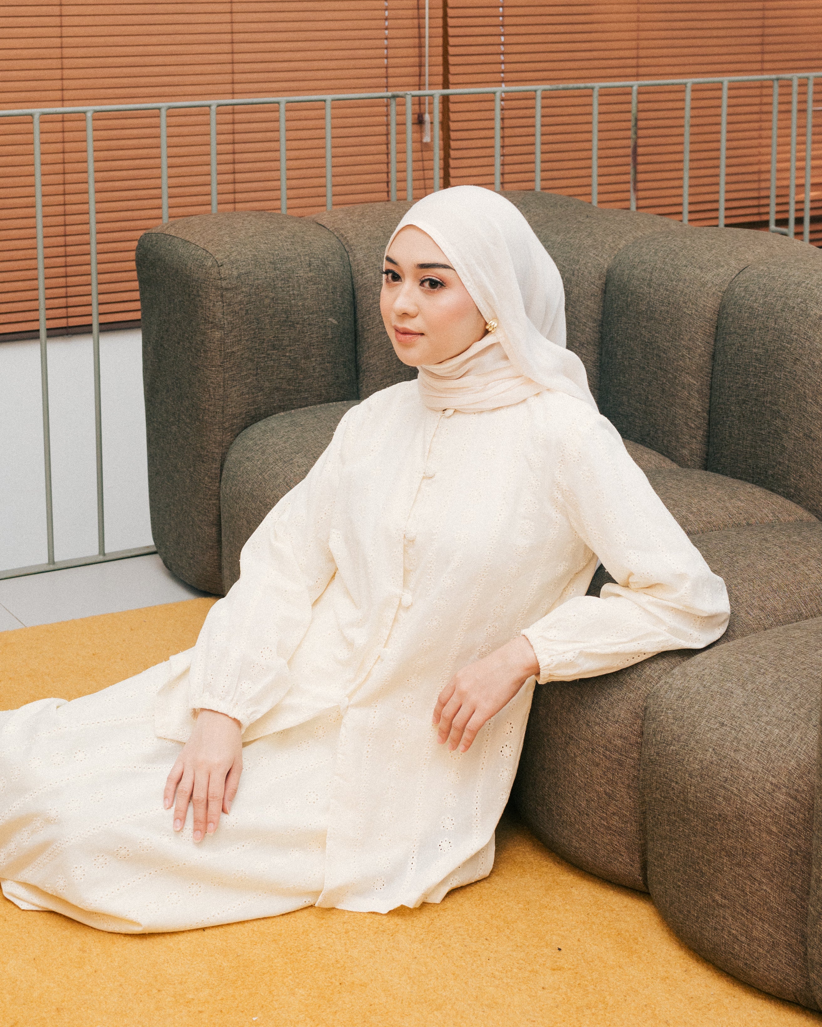Woman in a broken white tunic from Atala Scarves sitting on a brown couch with a neutral background