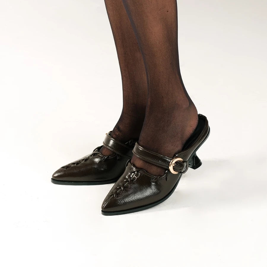Brown high-heeled shoes by Cekhas with decorative straps worn by a person on a white background