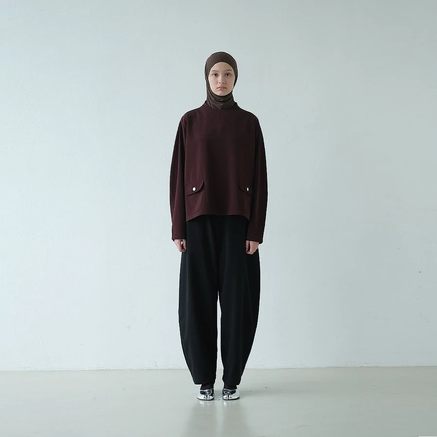 Person wearing a dark brown top with a hijab paired with barrel pants against a white background