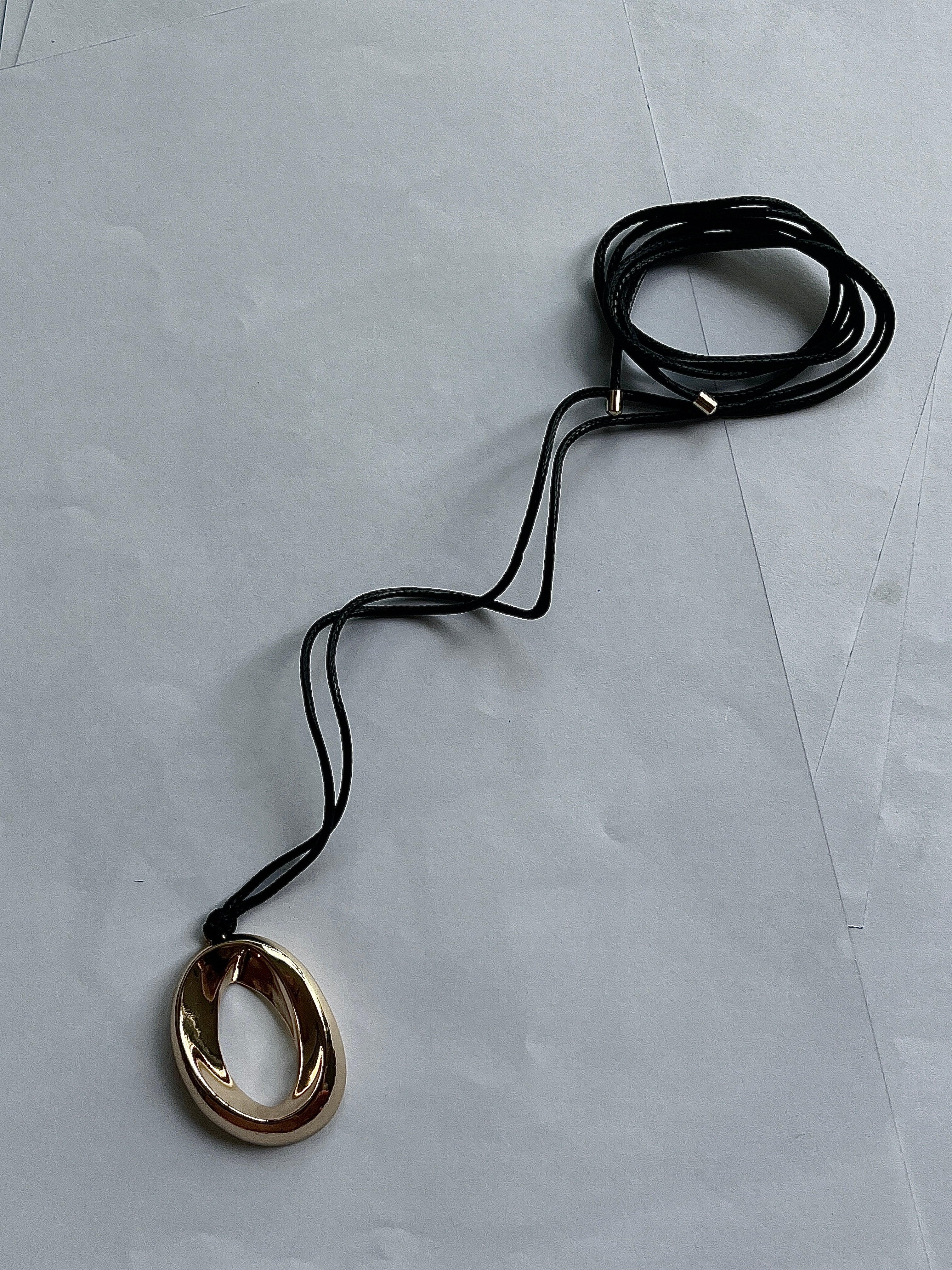 Gold pendant necklace by Darje on a black cord against a light gray background