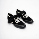 Pair of black shoes with decorative floral strap by Dianable on a white background