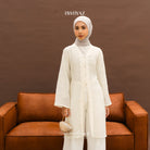 A woman wearing a white long-sleeve floral outer from BWBYAZ with a hijab, standing in front of a brown background.