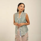 Woman wearing a light green sleeveless kebaya by Kartinis Label with floral patterns on a beige background