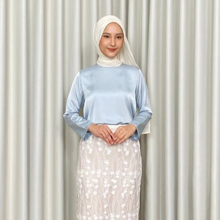Person wearing a light blue top by Kartinis Label and white floral skirt against a plain background