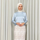 Person wearing a light blue top by Kartinis Label and white floral skirt against a plain background
