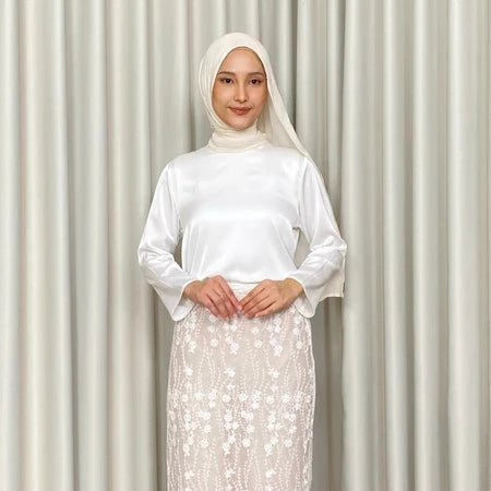 Woman wearing a white top by Kartinis Label with a hijab against a plain background